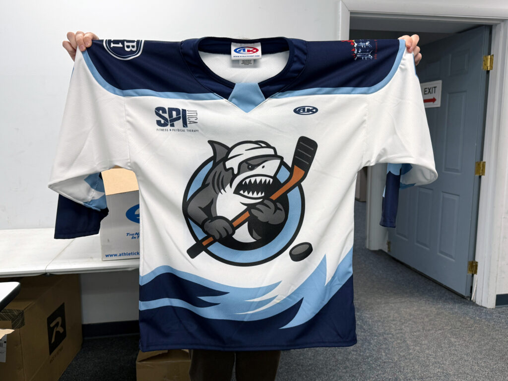 A photo of a blue and white Great White hockey jersey with a shark holding a hockey stick