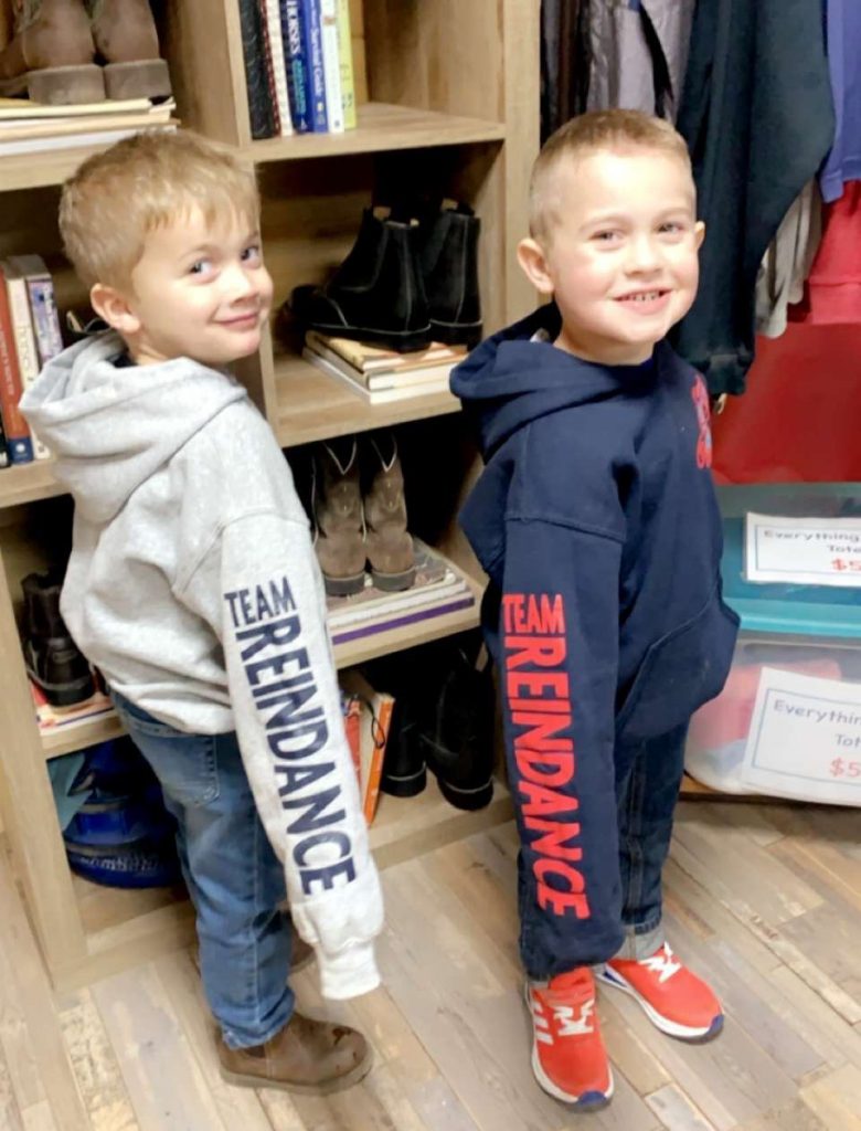 A photo of two kids showing off their screen printed sleeves that say "Team Reindance" in red lettering