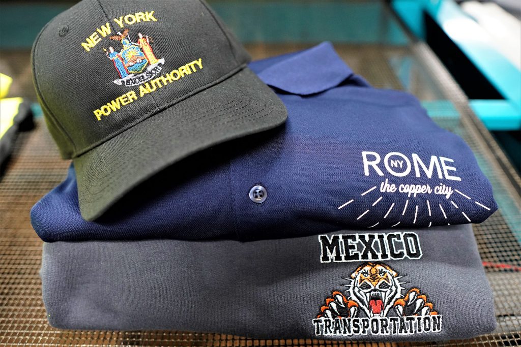 a photo of two shirts, one that says Rome, NY, The copper City and the other that says Mexico Transportation with a tiger and a baseball hat that says New York Power Authority on the front