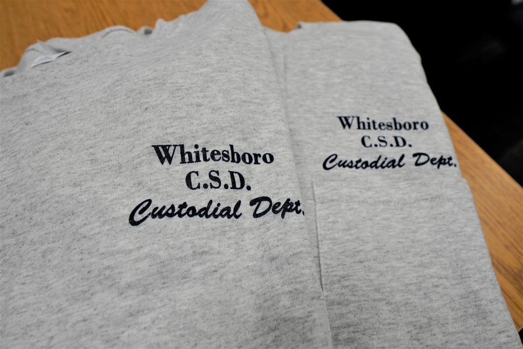 a photo of two grey t-shirts with pockets they say Whitesboro C.S.D Custodial Dept. in blue lettering